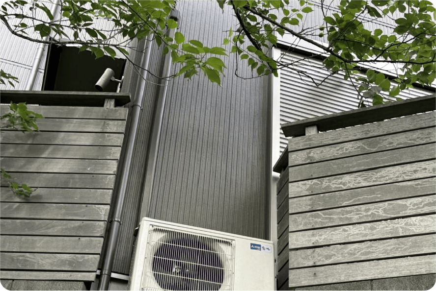 木塀や植栽に囲まれ作業スペースが限られた室外機の例。